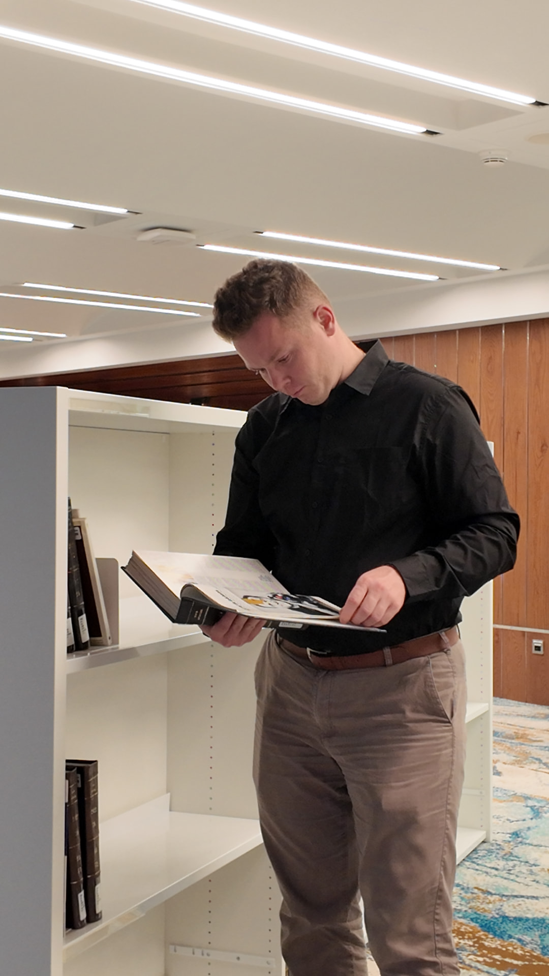 Nikita reading an architecture monograph beside library shelves